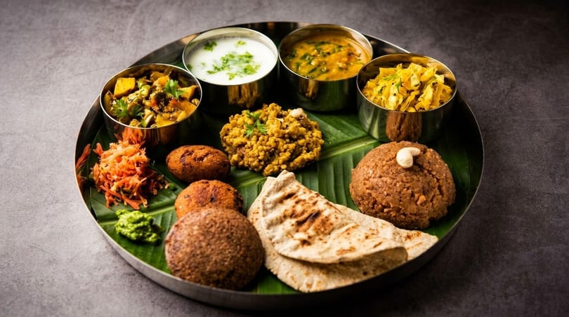 A traditional Indian thali meal with various dishes, including curries, flatbread, and sweets, served on a banana leaf.